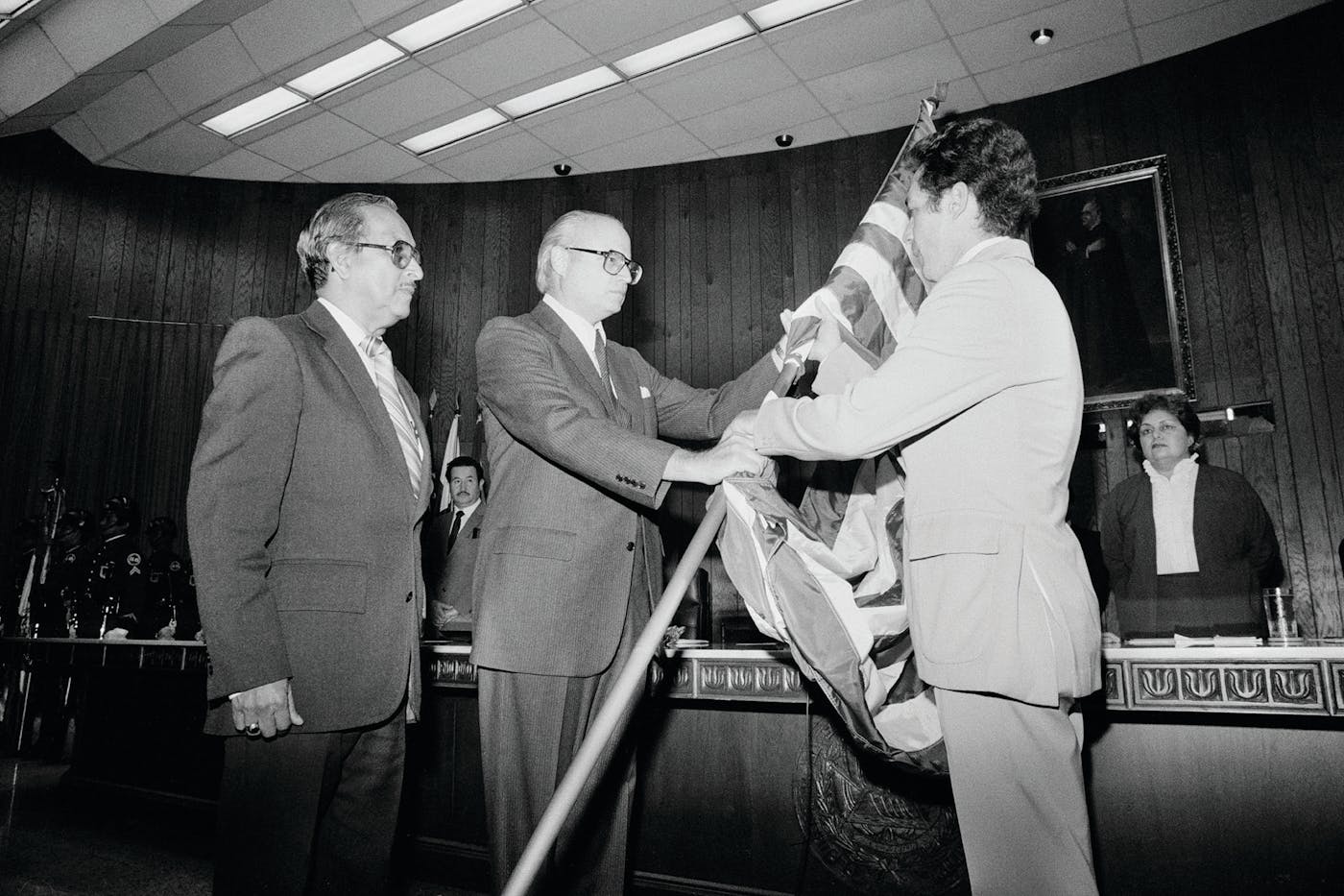Photo of: Ambassador Deane Hinton (center) handed a U.S. flag to Roberto D’Aubuisson, a Salvadoran national guard intelligence officer, in San Salvador in 1982.