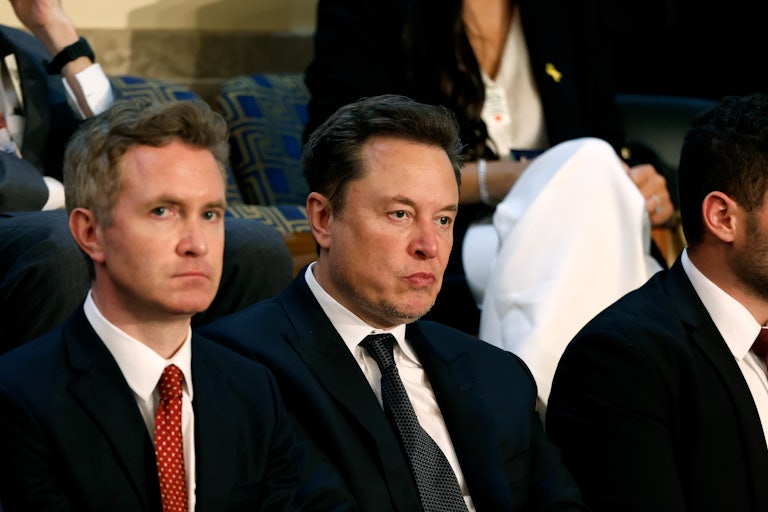 Elon Musk makes a weird face. He is seated near others.