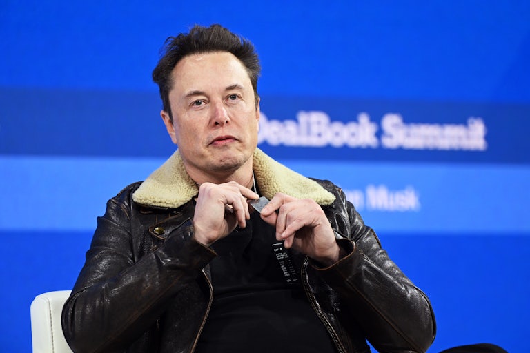Elon Musk sits and plays with his necklace in his hand