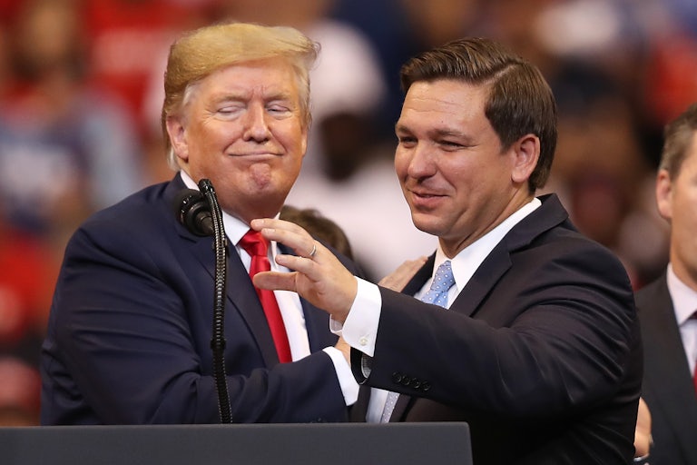 Donald Trump and Ron DeSantis smile and stand next to each other at a podium