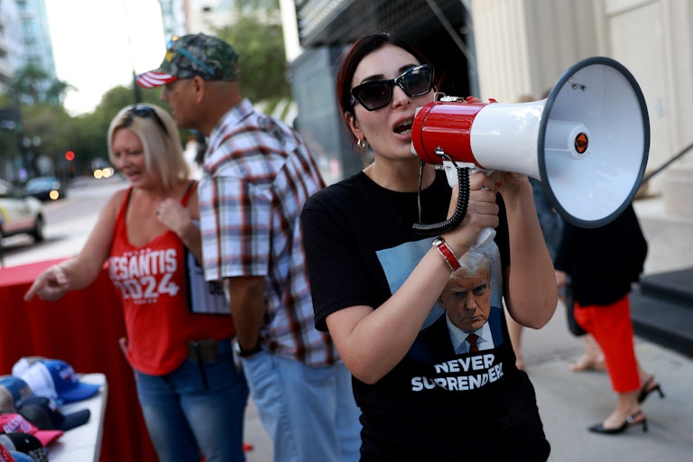 Laura Loomer wears a "Never Surrender" t-shirt with Trump’s mug-shot and speaks into a megaphone