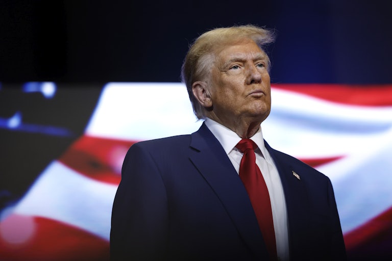Donald Trump stands in front of an image of an American flag